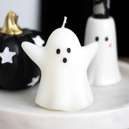 Ghost-shaped candle with black eyes and mouth on a white surface with Halloween decorations.