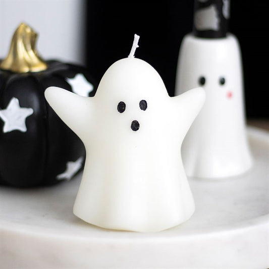 Ghost-shaped candle with black eyes and mouth on a white surface with Halloween decorations.